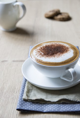 Tasse Cappuccino mit Kakao auf Holzplatte, Cookies und blauen Serviette  mit verschwommene Hintergrund