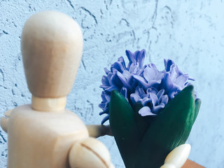 wooden faceless man gives blue flowers