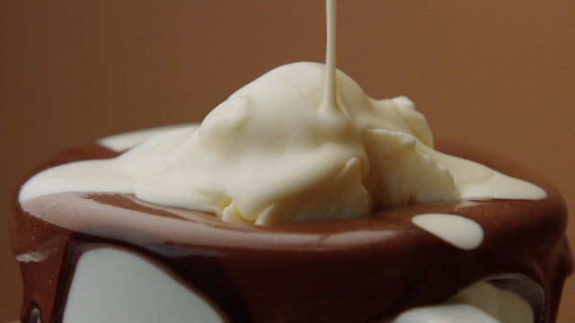 cup of hot chocolate with a cream and liquid white chocolate pouring on it. CLoseup