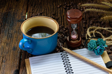 Fototapeta na wymiar Coffee cup with blank notebook, pencil, hourglass and coffee beans on wooden table