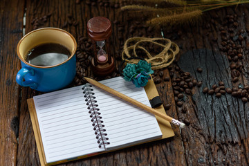 Blank notebook with pencil, coffee cup, hourglass and coffee beans on wooden table
