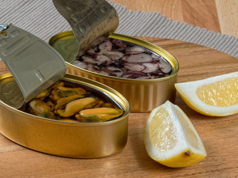 Cans of preserves with mussels and octopus with lemon slices, set on a rustic wooden board