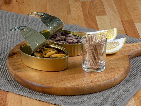 Cans of preserves with mussels and octopus on a rustic wooden board, with lemon slices and toothpicks
