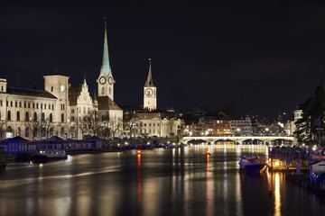 Fototapeta na wymiar Zürich bei Nacht, Fluss Limmat mit Reflexionen, Stadthaus, Kirchen Fraumünster und St. Peter, Münsterbrücke