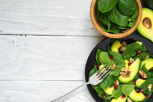 fresh salad with avocado, spinach, pomegranate and walnuts in black plate with fork. healthy food