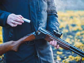 Sports shooting. Hunter reloading cartridge in field. Smoke from the trunks of smooth-bore hunting rifle after firing.
