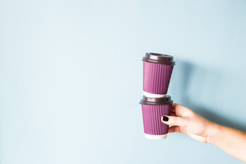 Purple paper kraft disposable cups for coffee with plastic lids in a female hand. One glass stands on the other. Tower of coffee. On blue background
