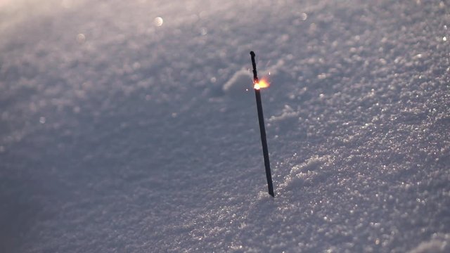 Thin and weak Bengal or Indian light, or sparkler, stick into snow and burning on gray background in slow motion, 240 fps. Pathetic and melancholy image.
