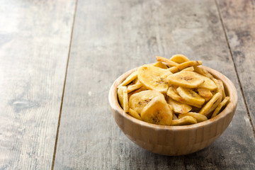 Banana chips in wooden bowl on wooden table background

