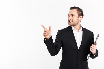 Successful businessman wearing black suit pointing finger aside and posing with folder in hand, isolated over white background copy space