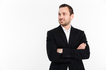 Portrait of young businessman looking aside while standing in suit with broad smile keeping arms folded, isolated over white background