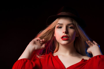 Pretty blonde lady with bright makeup and long hair posing in hat at studio