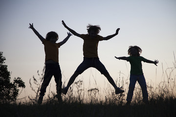 Children playing jumping on summer sunset meadow silhouetted