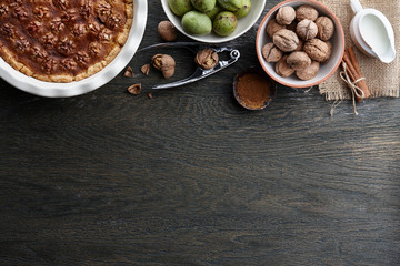 Traditional walnut pie, spices, nuts and nutcracker on dark wooden table, top view