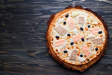 Delicious pizza with salmon, tuna and olives on wood, top view. Italian food, restaurant menu
