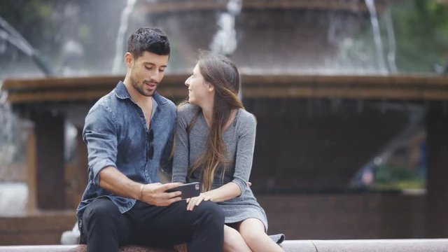 Happy young couple take pictures together in front of a fountain