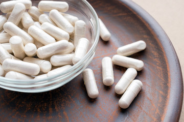 Veg herb capsules on round clay brown plate. Herbal Supplements Dangerous with Prescription Drugs....