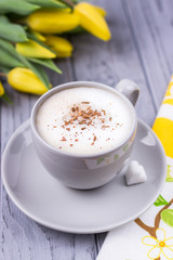 Coffee cappuccino with ceylon cinnamon and yellow tulips on a gray background