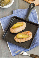 Appetizing appetizer. Homemade meat cutlets with pieces of salted cucumber on a black cast-iron frying pan on an old wooden table. 