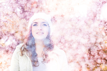 A girl in a warm hat and a knitted sweater, on a pink background with glare. Glamor and youth, snow or flowering. Aspiration, look up, smile, success and love. An inspiration and a positive attitude. 