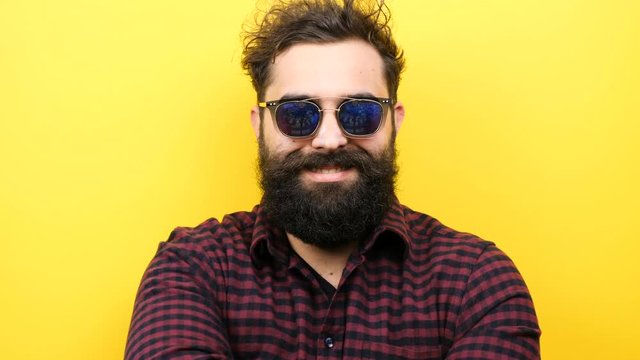 Smiling bearded hipster on yellow background with his sunglasses on