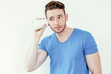 Concentrated young man eavesdropping with mug