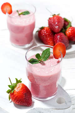 glasses of refreshing strawberry milkshake on white table, vertical