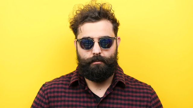 Long bearded man puts his sunglasses on from the top of his nose on yellow background