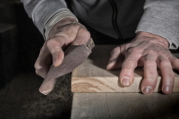 Detail of male hand using a sanding block to sand timber desk