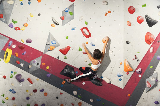 Woman practicing rock climbing on artificial wall indoors.