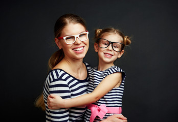 Happy smiling female with little girl changing eyeglasses with each other. Eye care concept.