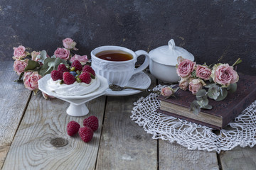 Obraz na płótnie Canvas on a wooden table are a cup of tea, sugar bowl, roses, raspberries, cake and heart from lace