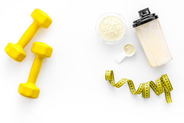 Nutrition for muscle growth. Scoop of protein near shaker and dumbbell on white background top view