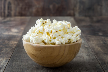 Popcorn in bowl on wooden table background.