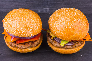 Two homemade burger with chop and baked vegetables on a dark background