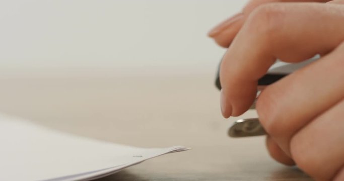 Macro shooting of the female hand doing holes in the papers by stepler. Close up