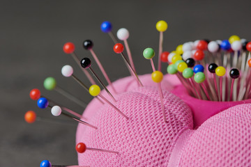 pink needle cushion with a lot of colored pins in it