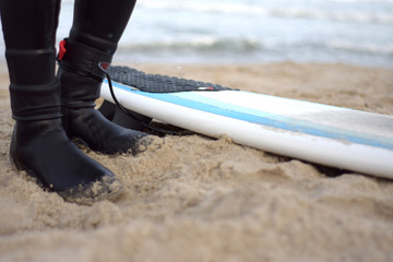 Surfer. Surfing. Watersport. black wetsuit and surfboard. sand and ocean, legs in black shoes.