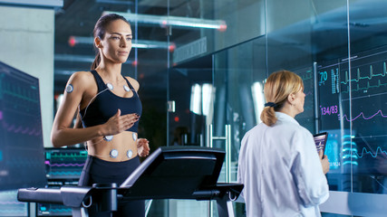 Beautiful Woman Athlete Runs on a Treadmill with Electrodes Attached to Her Body, Female Physician...