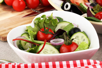 bowl of salad with vegetables and greens, with tomato, cucumber and onions.
