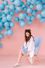 Beautiful girl in a blue dress in a pink room with blue balls and a blue armchair