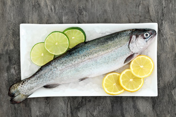 Rainbow trout health food on crushed ice with lemon and lime fruit on marble background. Very high...