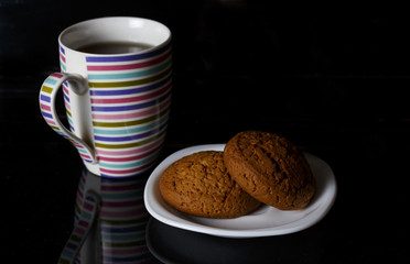 Cup with tea and two oatmeal cookies on a black background