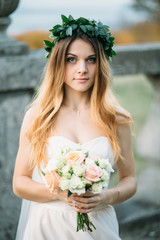 Stunning bride stands with a bouquet on a ruined balcony