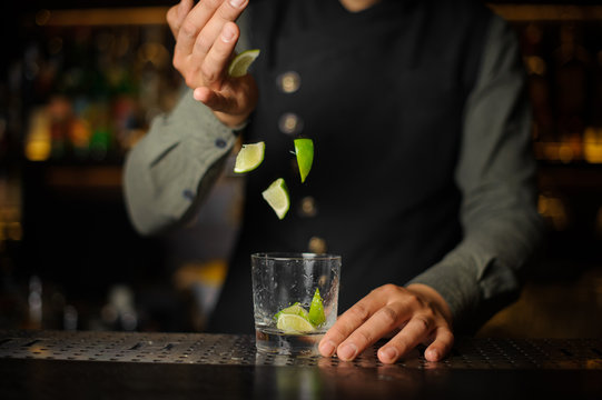 Bartender adding pieces of lime into the cocktail glass. Process of making Caipirinha cocktail