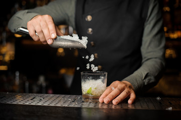 Bartender adding ice cubes into the cocktail glass. Process of making Caipirinha cocktail