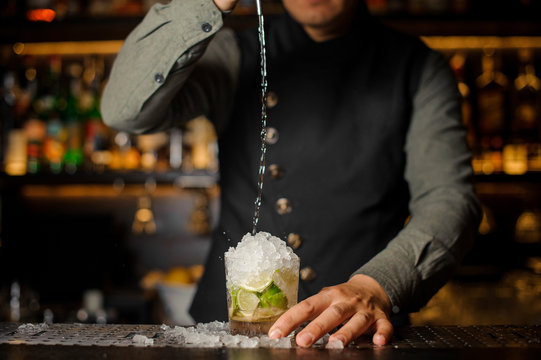 Barman pouring cachaca into the cocktail glass. Process of making Caipirinha cocktail