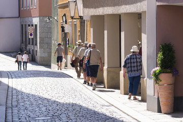 Backside view of seniors walking along small street in summer