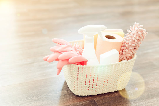 set of cleaning products, sponges and gloves in a white plastic basket, on a wooden floor, a sunbeam