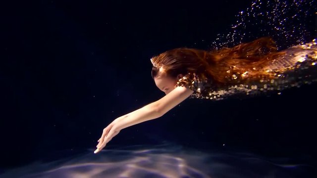 Side view shot of a adorable red haired little girl dressed like a mermaid swimming underwater.